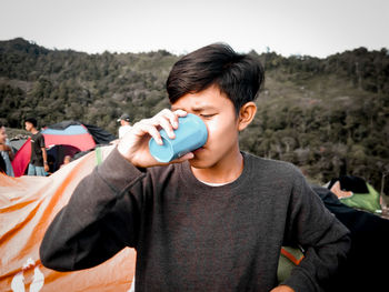 Portrait of young man holding camera against sky