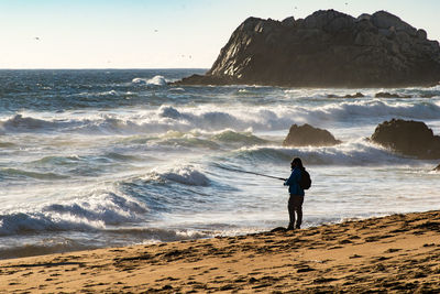 Full length of man fishing on beach against sky