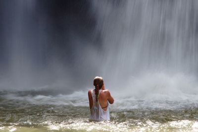 Rear view of woman standing in river by waterfall