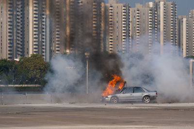 Burning car on road against buildings in city