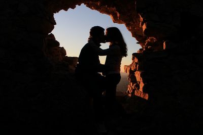 Silhouette people standing on rock formation against sky