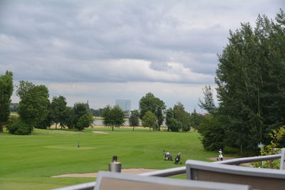 Scenic view of green golf course against cloudy sky