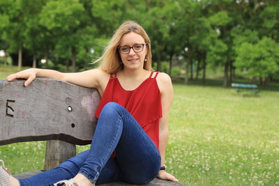 Portrait of smiling young woman sitting on bench in park