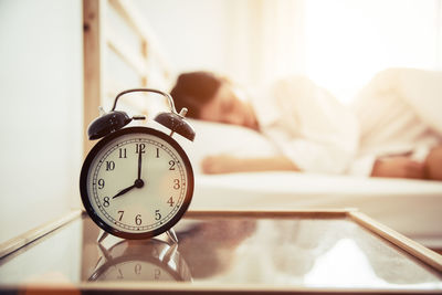 Close-up of alarm clock on table by woman sleeping on bed at home