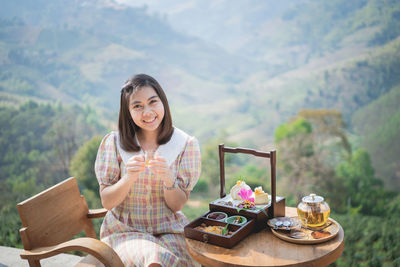 Portrait of smiling woman holding ice cream against mountains