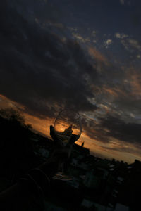 Man holding umbrella against sky at sunset