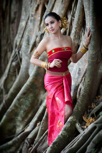 Woman in traditional clothing standing by tree trunk