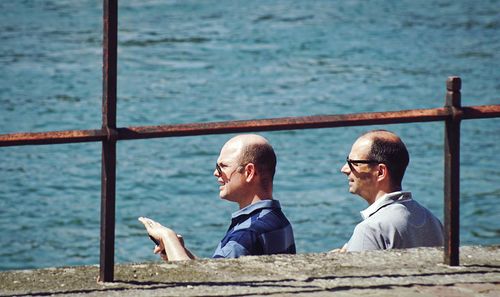 Rear view of two men sitting by sea
