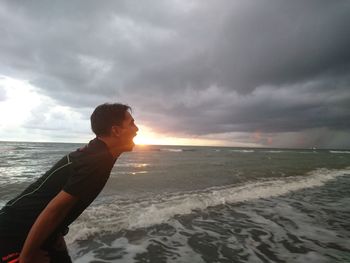 Optical illusion of man eating sun at beach against cloudy sky