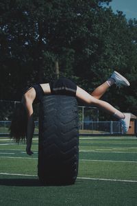 Full length of woman lying on tire at field against trees