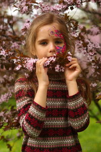 Spring portrait of a six year old girl with a facepaint standing under the blooming pink cherry tree