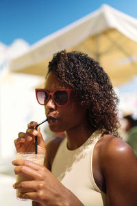 Portrait of young woman drinking water against sky