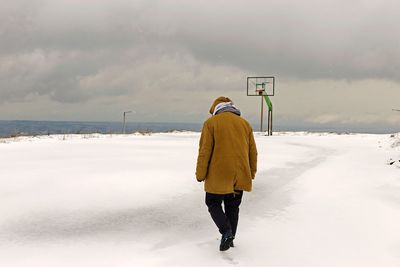 Rear view of man walking on snow covered landscape