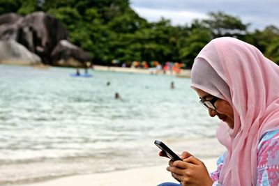 Close-up of man holding mobile phone at beach