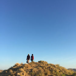 Rear view of people walking on mountain against clear blue sky