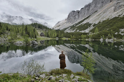 Rear view of monk standing by lake with mountains reflection