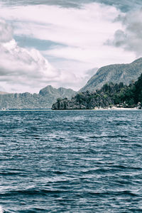 Scenic view of sea by mountain against sky