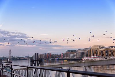 Hot air balloons over river and buildings against sky at dusk in city