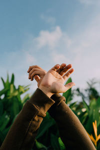 Close-up of hand against plants and sky