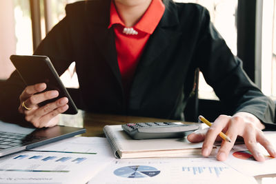 Midsection of woman using mobile phone while sitting on table