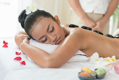 Midsection of masseuse standing by young woman sleeping at spa
