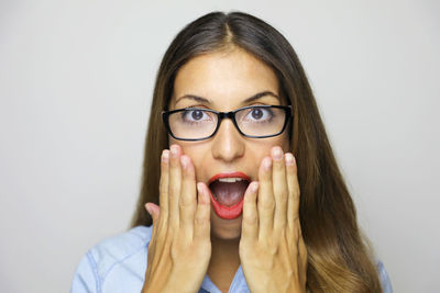 Close-up portrait of shocked young woman wearing eyeglasses against gray background