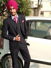 Portrait of young man standing wearing suit while standing by car