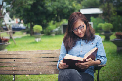 Young woman reading book while sitting on park bench