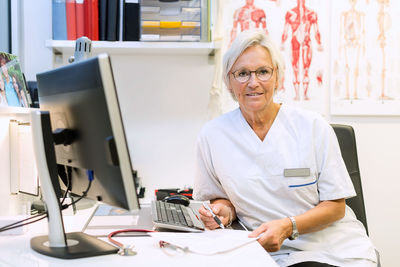 Portrait of confident orthopedic surgeon sitting at computer desk in clinic