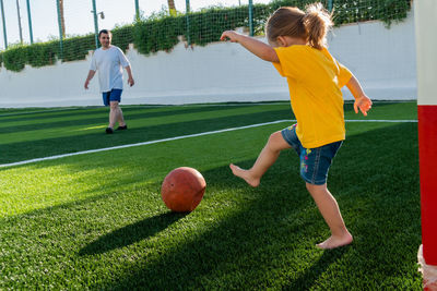 Cute little girl kicking soccer ball to father while standing in gateway