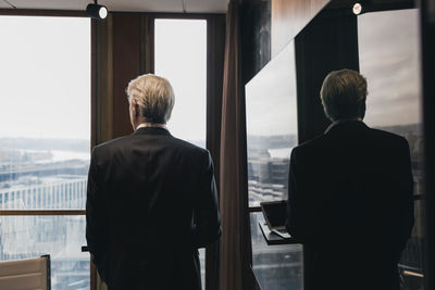 Rear view of senior businessman standing by reflection on television in board room