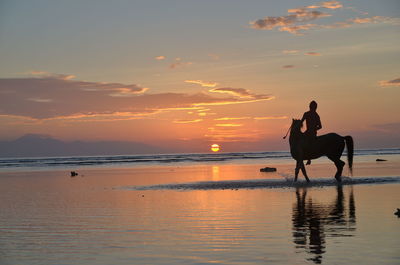 Silhouette woman on horse at beach against sky during sunset