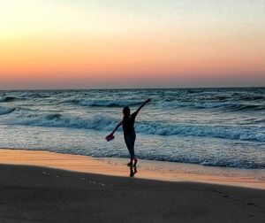 Full length of woman walking on beach against sky during sunset