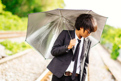 Young man holding umbrella while standing on railroad track
