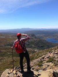 Rear view of man standing on rock at mountain against sky