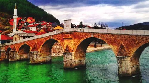 Arch bridge over river against sky in city