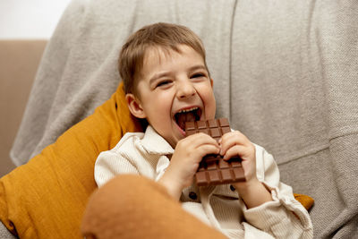 Little adorable boy sitting on the couch at home and eating chocolate bar. child and sweets