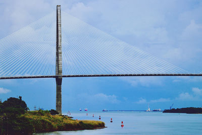 Suspension bridge over sea against cloudy sky