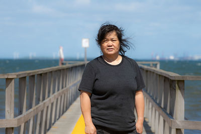 Portrait of teenage girl standing on bridge against sky