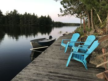 Chairs on lake by trees against sky