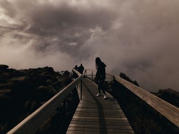 Rear view of man walking on footbridge against sky