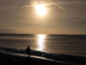 Silhouette woman on beach against sky during sunset