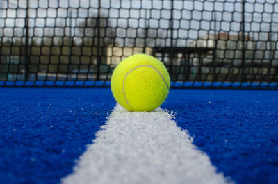 Selective focus, a ball on the line of a blue paddle tennis court, racket sports concept