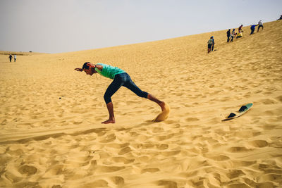 Side view full length of man sandboarding at desert