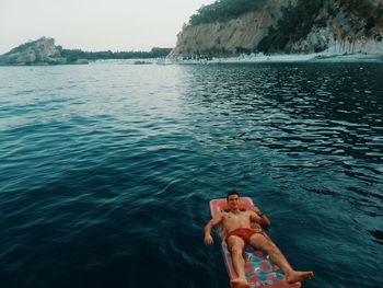 Full length of shirtless man relaxing on inflatable raft at sea