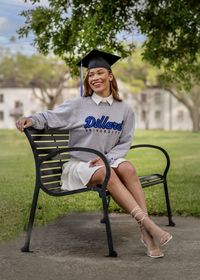 Portrait of graduating student sitting on bench in her cap smiling 