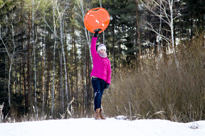 Full length of teenage girl holding toboggan while standing on snow