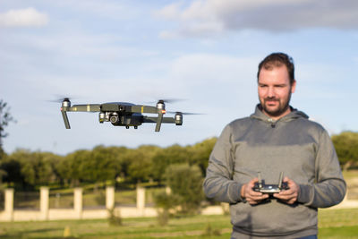 Smiling man flying drone against sky