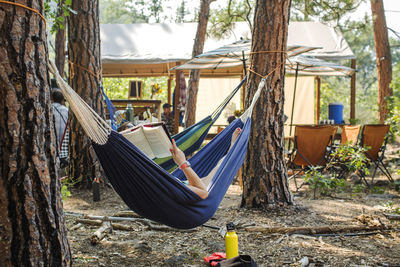 A woman reads a book in a hammock at a glamping camp scene