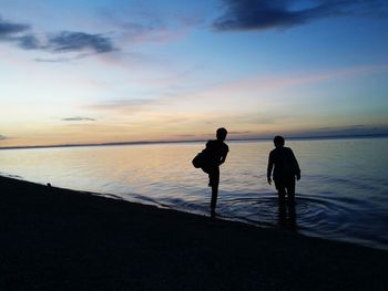 Silhouette friends standing on beach against sky during sunset